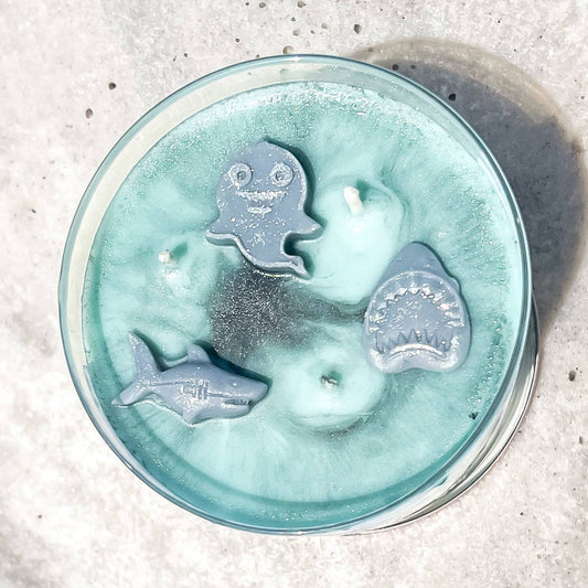 Candle with shark-shaped wicks in a glass container on a textured surface