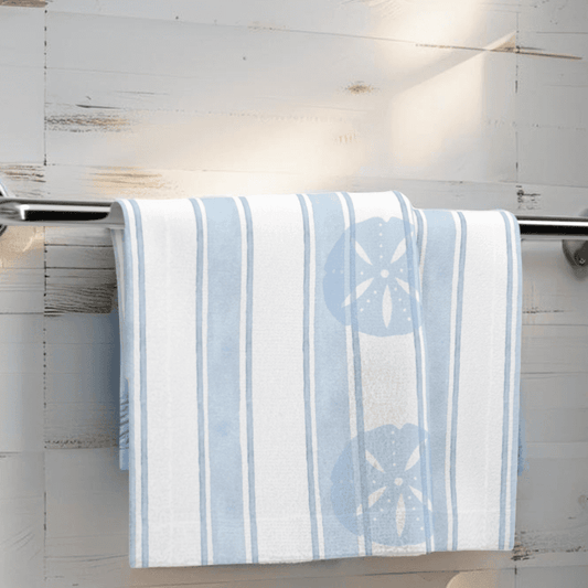 Light blue coastal face towel with sand dollar design hanging on rack in beach-themed bathroom.