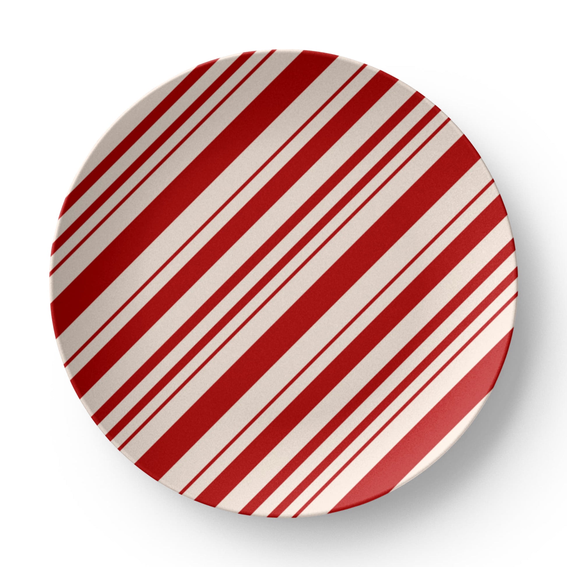 Red and white striped holiday plate set on a wooden table with a full festive Christmas dinner setting.