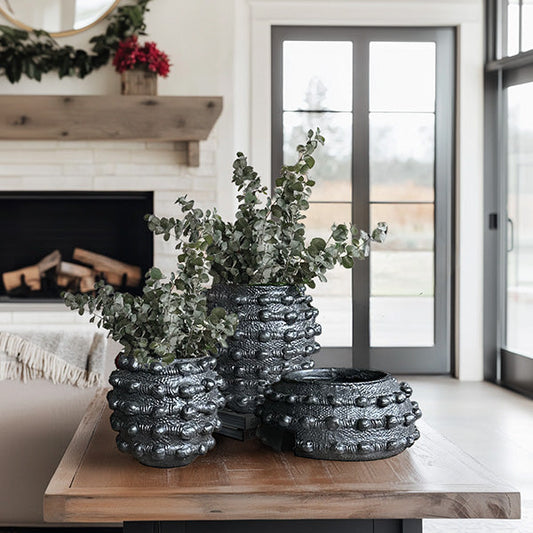 Decorative black textured planters with greenery on a wooden table in a living room.
