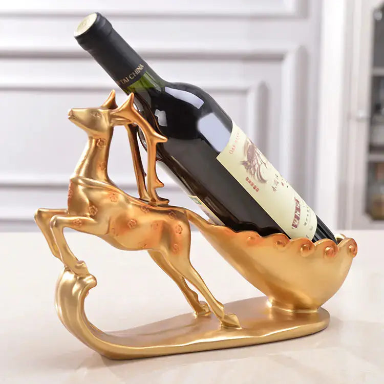 Gold deer-shaped wine bottle holder with a red wine bottle on a white surface.