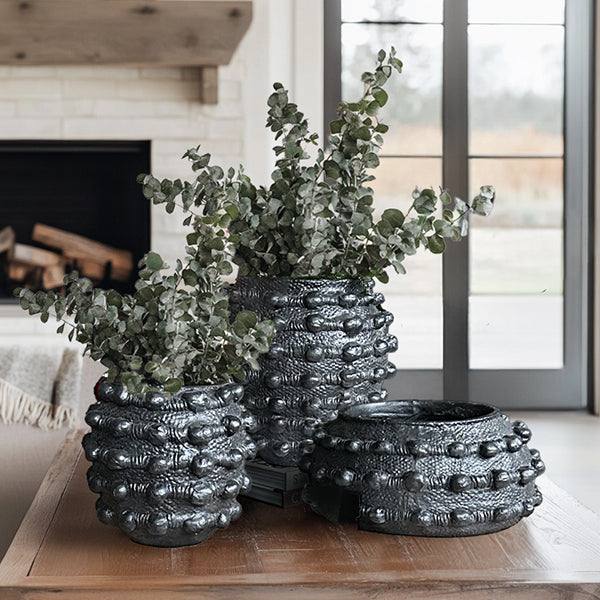 Handcrafted matte black textured planter set displayed outdoors with green plants