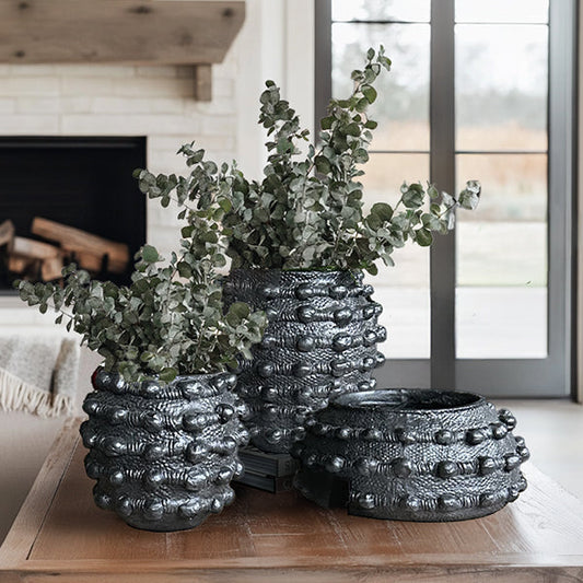 Handcrafted matte black textured planter set displayed outdoors with green plants
