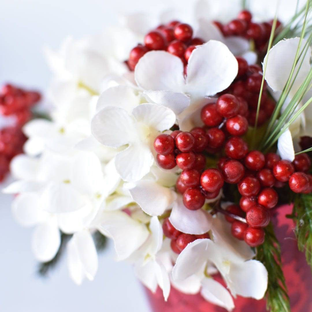 Holiday mantle decor featuring a white hydrangea arrangement in a red glass vase.