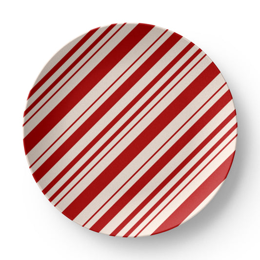 Red and white striped holiday plate set on a wooden table with a full festive Christmas dinner setting.