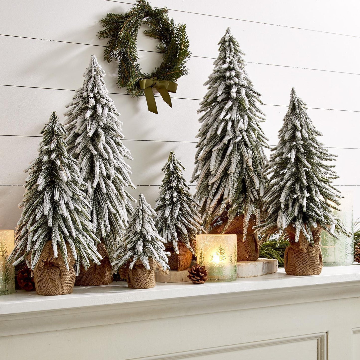Set of 6 snow covered miniature flocked Christmas trees with jute bases for mantle display.
