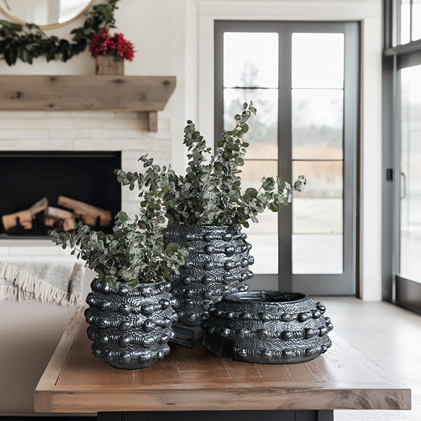 Decorative black textured planters with greenery on a wooden table in a living room.