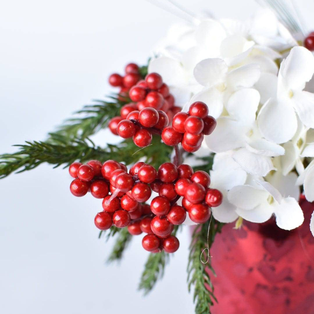 Close-up of winter greenery and white hydrangea stems in a vibrant red glass container.